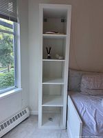 Full view of white Ikea bookshelf with four open shelves against wall near window.