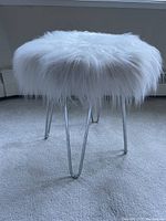 Side angle showing white faux fur upholstery and polished silver metal hairpin legs on carpeted floor.