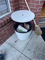 White outdoor cooler with screw-on lid removed and used as a small table. Cooler contains various tools and cleaning items.