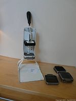 Full view of 1940s Becky Porter potato French fry cutter with stand on wooden surface and 4 stainless steel cutting dies laid out beside it.