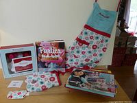Full lot showing apron, oven mitt, spatula, cookbook and two paper craft kits on table