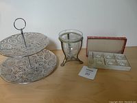 Photo showing two-tiered metal dessert server, brass holder with crackled glass insert, and boxed set of 6 crystal salt dishes.