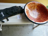 Charbroil leather BBQ gloves laid next to large orange glass mosaic bowl on a table.