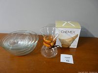 Photo showing Chemex coffee carafe with wooden collar, box of coffee filters, and set of nesting glass bowls.