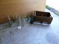 Photo of all items showing 12 bottles, 4 glasses, and 1 wooden crate with Coca-Cola branding on concrete floor.