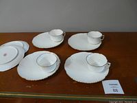 Photo of four bone china lunch plates each paired with matching cups, two spare plates beside them on wood surface