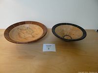 Two handcrafted wooden bowls placed side by side on a wooden surface, displaying size difference and rim segmentation