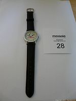 Full view of the Monopoly wristwatch with black strap and silver casing laid flat on a white surface.