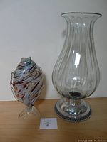 Clear glass vase with silver metal base beside colorful swirled glass fish figurine, full view showing both items.
