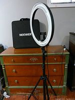 Neewer selfie ring light mounted on tripod with carrying case behind it on wooden dresser.