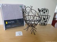 Full lot showing new curtain in packaging, metal wire bowl with birds, and butterfly wall decor holder on wooden table.