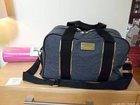 Gray Puma gym bag with black straps and gold accent zippers alongside rolled pink yoga mat on a wooden surface.