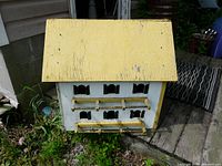 Front and side of the wooden Purple Martin house showing the yellow roof, multiple entrance holes, and white body with perches.