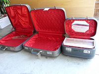 Full view of all three vintage Futurama suitcases open, showing red quilted interiors, one with a dent, key inserted in one lock