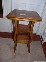 Front angled view of small wooden side table showing top, two shelves, and curved legs.