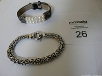 Photo of two bracelets, one sterling silver Byzantine chain bracelet and one pearl leather bracelet with taped strap, along with MaxSold lot card