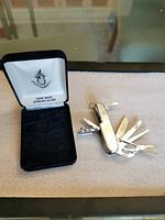 Multi-tool pocket cutter open showing multiple stainless steel tools and original black velvet box with logo inside the lid