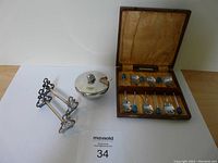 Photo of the coffee spoon set in original case, mustard server, and cutting tool rests on a white surface
