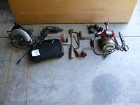 Photo showing the full lot of assorted power and hand tools arranged on a concrete floor.