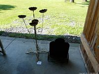 Full view of the metal African violet plant stand with five flower-shaped holders and metal scroll base, alongside the metal wall planter on ground.