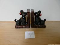 Front view of the matched pair of black poodle dog bookends facing each other on a wooden surface with a white background.