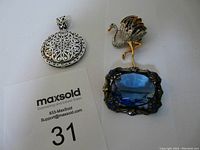 Three-piece vintage jewelry lot including a sterling silver pendant, a blue glass stone brooch, and a crystal encrusted ostrich brooch shown together.