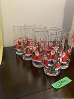 Photo of six clear tall glasses with Christmas themed printing of Santa and snowmen, arranged in a row.
