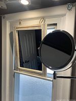 Two small mirrors on a window: a rectangular wood-framed hanging mirror with a rope and a round, dual-sided metal wall-mounted shaving mirror