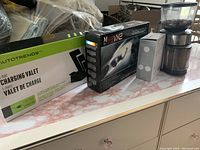 Photo showing boxed charging valet, boxed Migo VX2 car light, boxed clip LED lamp, and electric coffee grinder on dresser surface.