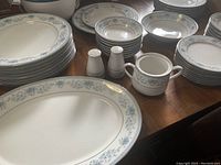 Wide shot of assorted plates, bowls, salt and pepper shakers, and sugar bowl with a blue floral pattern and gold trim on white base.