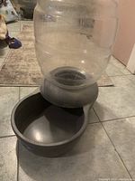 Self-watering dog water bowl with clear reservoir and gray base bowl on tiled floor