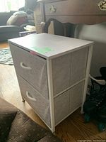 Tall shoe rack with four fabric shelves and white metal frame for storage, positioned beside a wooden table on a hardwood floor.