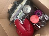 All items packed together in a box: red panini press, assorted small blenders including silver and black blender, purple blender, blender jars, and appliance cords.