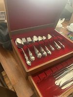 Opened wooden case showing 6 large forks and 6 large spoons seated in red velvet compartments, ornate pattern on handles visible