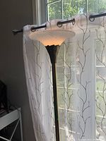 Full view of the floor lamp with a white textured glass shade and dark metal stand near the window.