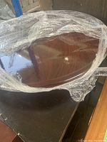 Top view of one disassembled walnut end table top wrapped in plastic.