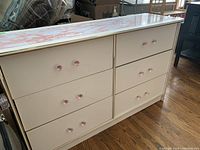 Front view of the white dresser showing six drawers with pink acrylic knobs and faux marble top surface.