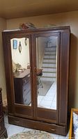 Front view of wood armoire showing two full-length mirrors on doors and bottom drawer.