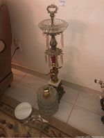Wide shot of Oriental or Victorian style ornate stand with crystal ashtray on top, onyx lighter beside, and two additional ashtrays on the floor.