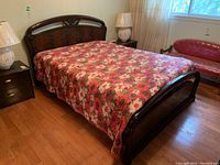 Full view of lacquered wood bed with floral bedspread, side tables, and nearby furniture