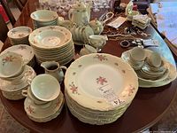 Full view of china set displayed on a table showing stacked plates, bowls, teapot, creamers, cups, and saucers all featuring floral designs and gold rims.