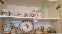 Top shelf with six Prince Charles and Diana coffee mugs, two plastic jugs to the right
