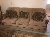 Front view of a three-seat beige fabric couch with three seat cushions and four patterned throw pillows.