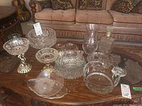 Full overview of glass and crystal items on wooden table showing bowls, vases, and jar items in need of cleaning.