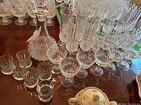 Photo showing crystal decanter, multiple flute glasses, shot glasses, smaller glasses, all with intricate cut patterns.