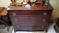 Wood dresser front view showing three large drawers with brass handles and scratches on the surface.
