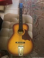 Full body of the Harmony Stella acoustic guitar laid flat, showing sunburst finish, wooden pickguard, and metal tailpiece.