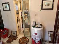 Wide view of room corner with framed prints on walls and various items on floor including plates and clock