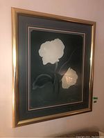 Framed botanical print with white flower on dark green background in gold-tone frame.