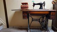 Full side view of the vintage Singer treadle sewing machine on wooden table with drawers and iron treadle base